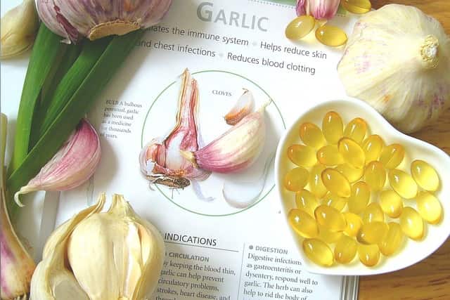 Raw garlic and garlic supplements in a small heart-shaped bowl with a document in the background indicating the benefits of garlic